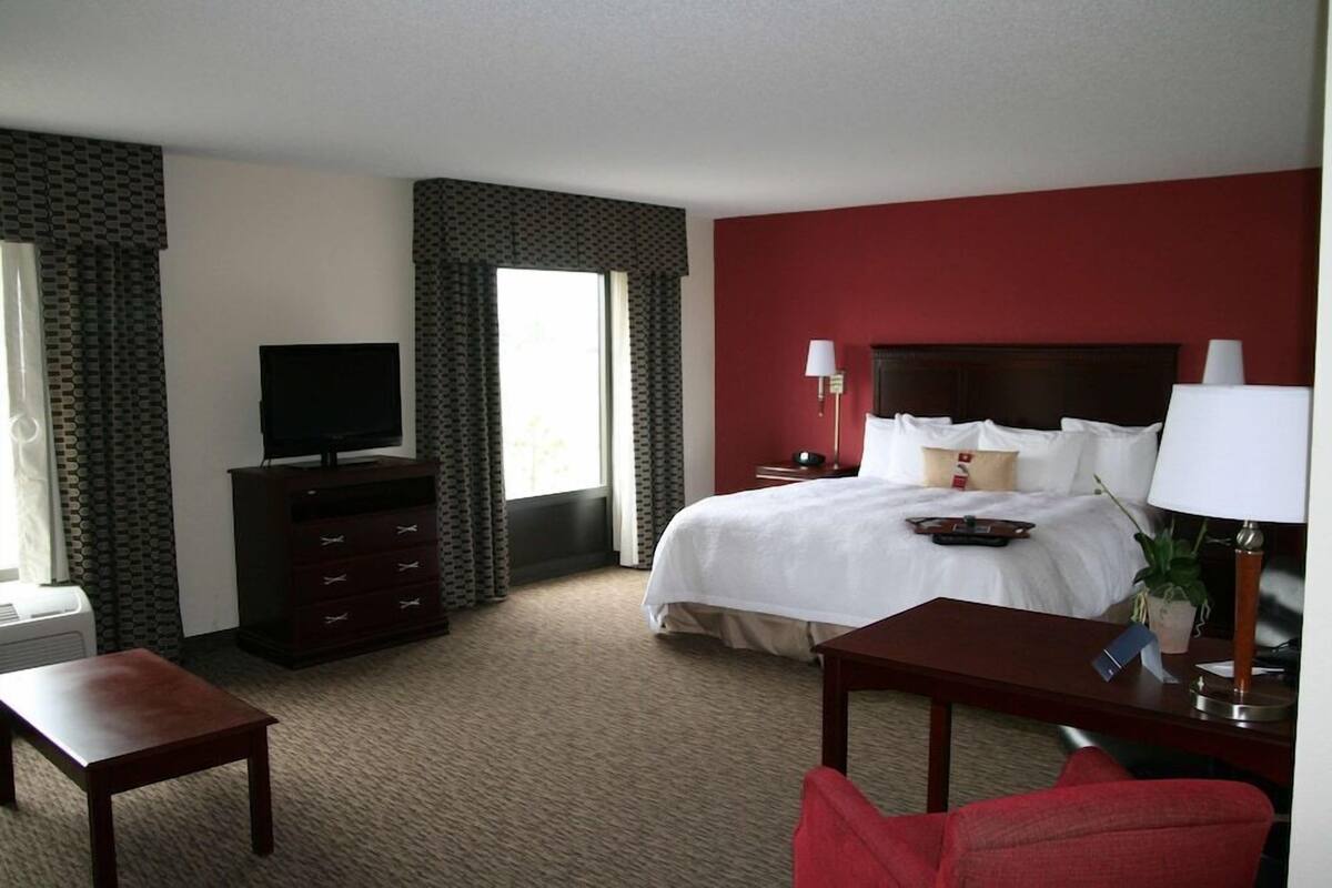A hotel room with a bed, a TV, a desk, a chair, a dresser, and a lamp.