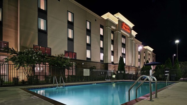 A hotel with a swimming pool, a fenced area, and a sign indicating it is a Hampton Inn Suites location.