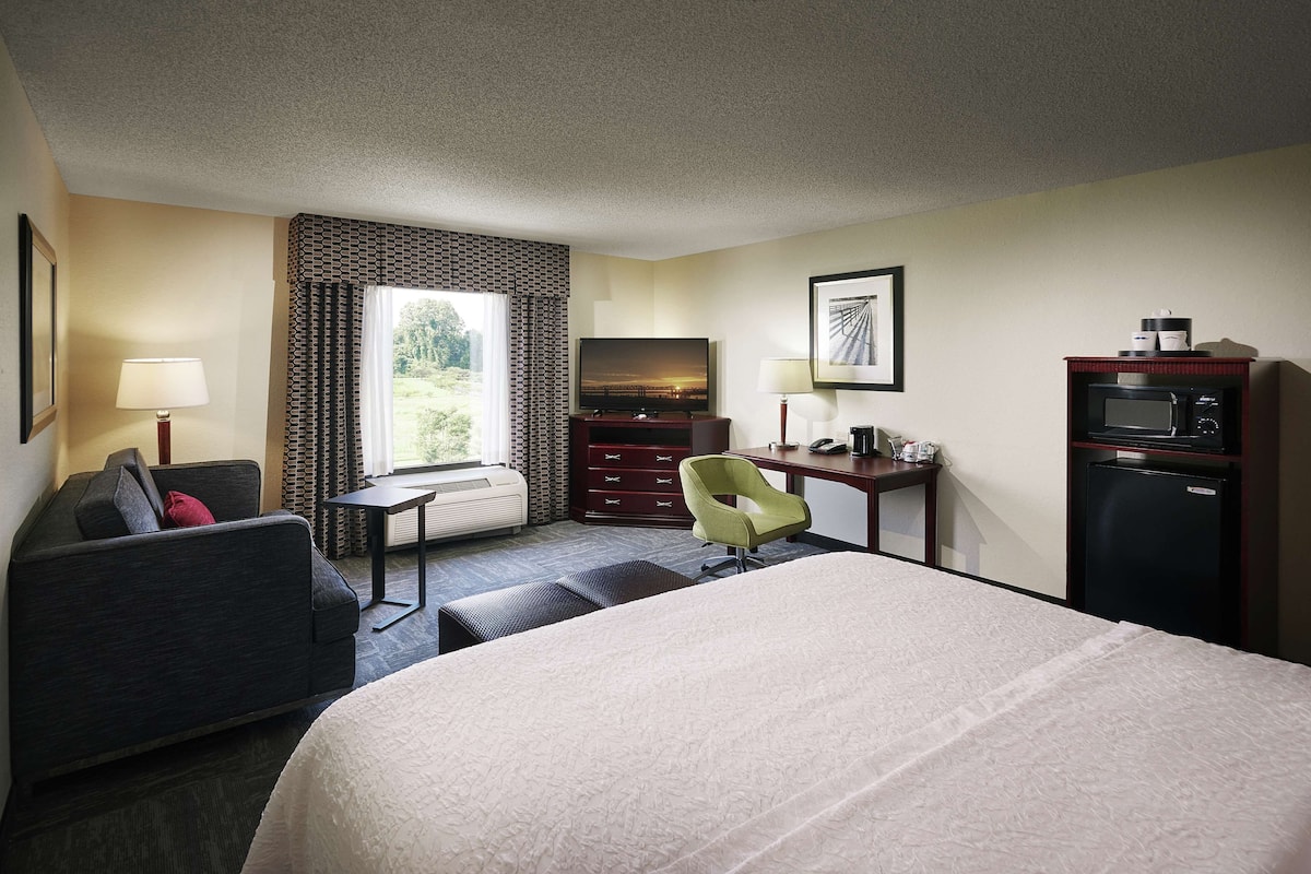 Habitación de hotel con cama, escritorio, silla, televisor, microondas y ventana con cortinas.