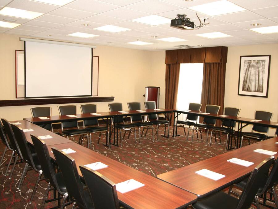 A conference room with a long table, multiple chairs, a projector screen, and a carpeted floor.