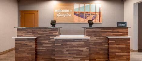 Un mostrador de recepción con un cartel que dice 'welcome to Hampton', dos lectores de tarjetas y un cartel de 'Hilton Honors'.