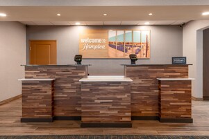 Un mostrador de recepción con un cartel que dice 'welcome to Hampton', dos lectores de tarjetas y un cartel de 'Hilton Honors'.