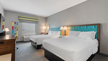 Habitación de hotel con dos camas, un escritorio, una silla, un ventanal y una pared con obras de arte coloridas.
