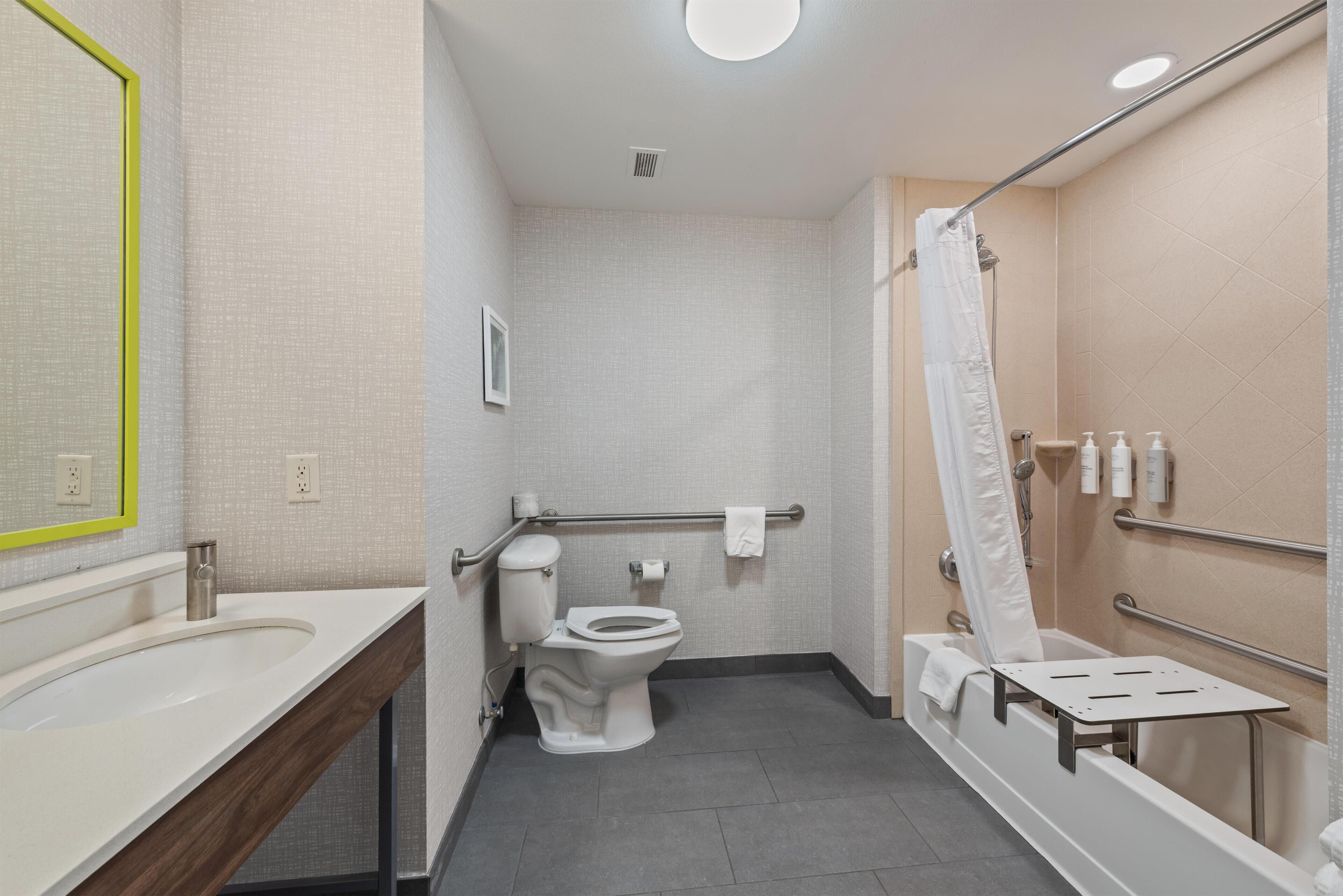 A bathroom with a toilet, sink, shower, and grab bars.
