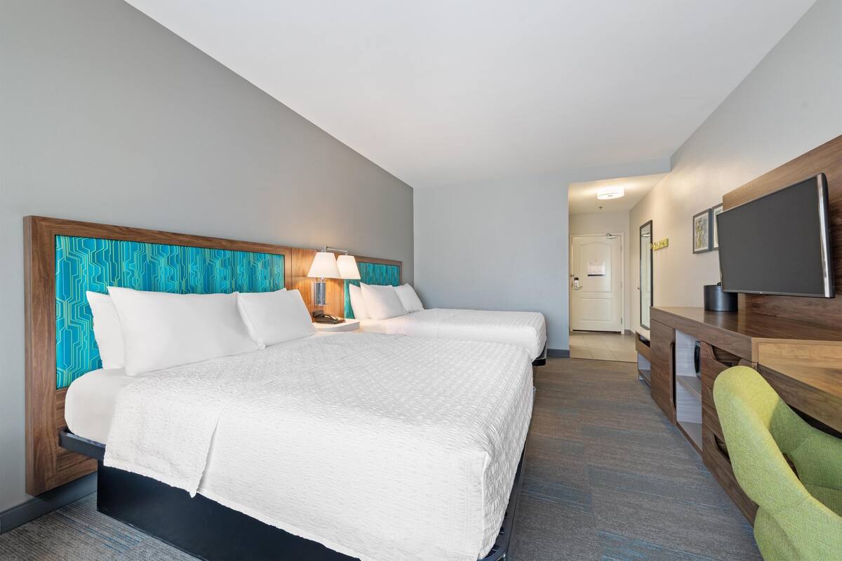 A hotel room with a bed, two bedside tables, a desk, a chair, and a television.
