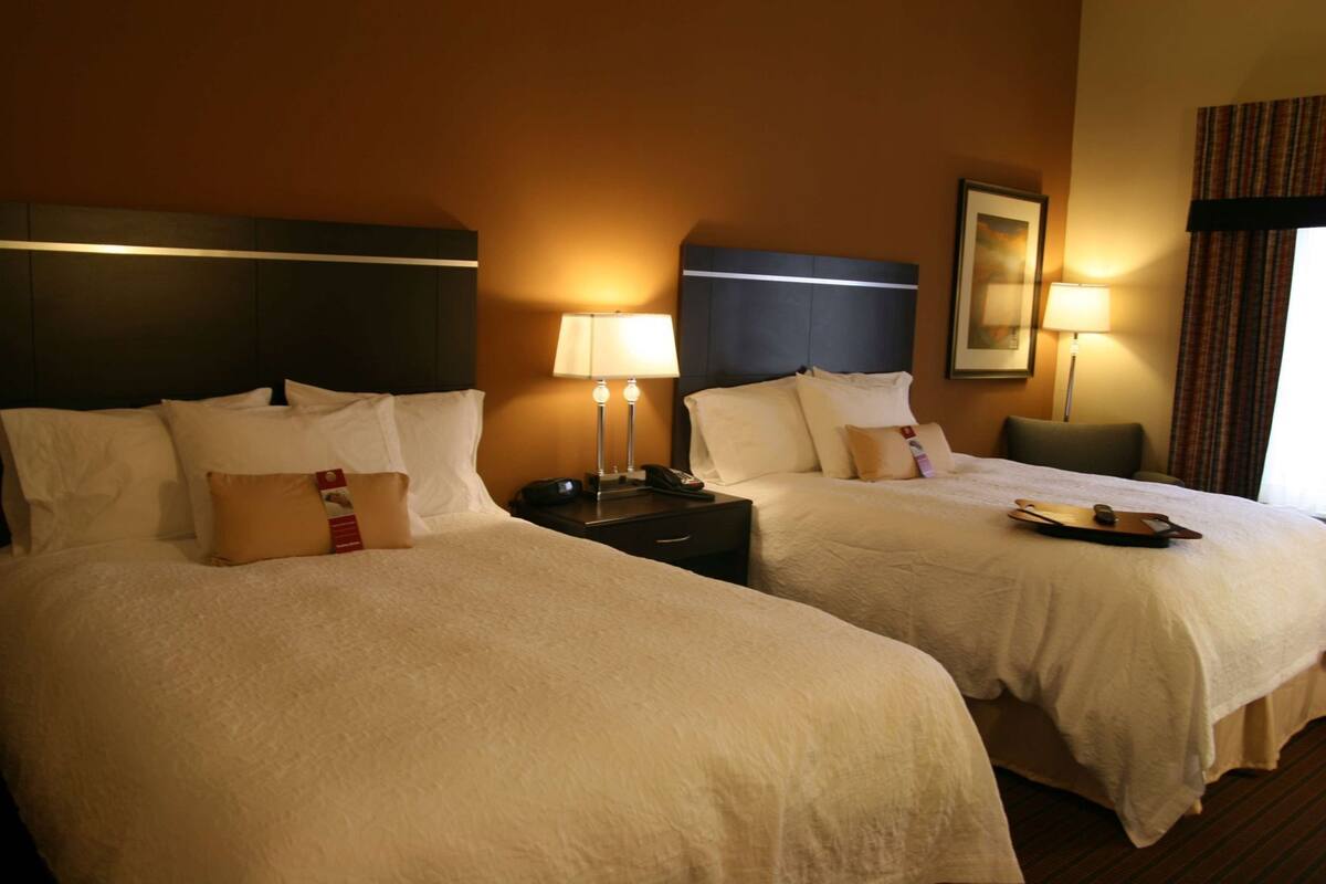 A hotel room with two beds, nightstands, lamps, a framed picture, and a window with curtains.