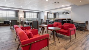 A spacious lounge area with red sofas, round tables, and a dining area with chairs and a counter. - Hampton Inn La Junta (La Junta)