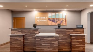 A reception desk with a 'Welcome to Hampton' sign, a wooden panel design, and a 'Hilton Honors' logo. - Hampton Inn La Junta (La Junta)