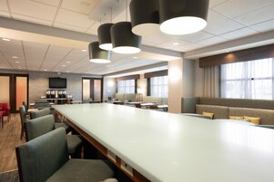 A modern hotel lobby with a long reception desk, seating area, and a television screen.