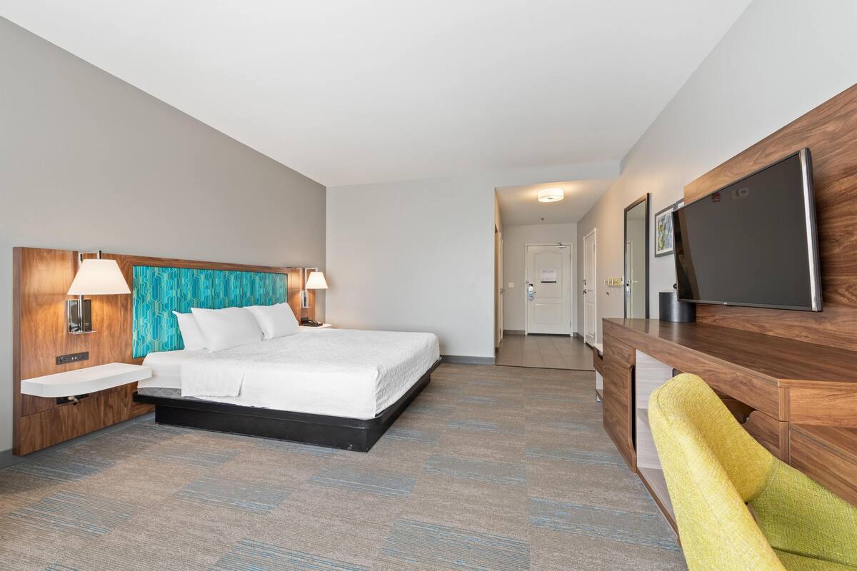 A hotel room with a bed, bedside lamps, a flat-screen TV, a wooden desk, and a chair.