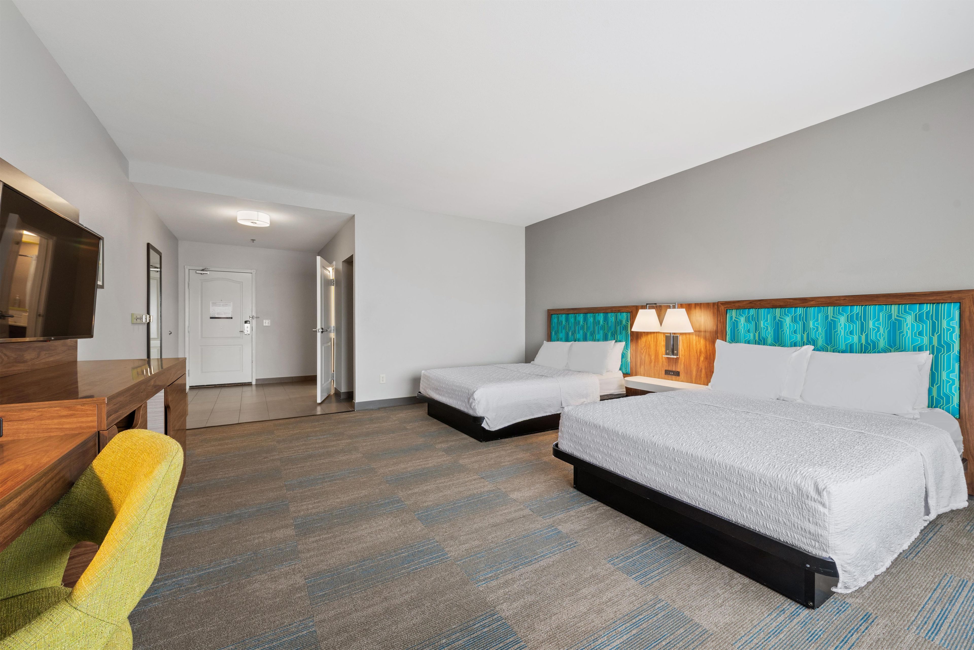 Una habitación de hotel con dos camas, un escritorio, una silla, un televisor y un baño.