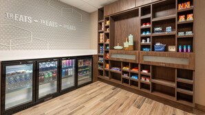A refrigerated beverage display, snack shelves, and a wall with 'TREATS' signage. - Hampton Inn La Junta (La Junta)