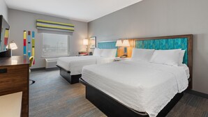 A hotel room with two beds, a desk, a chair, a window with a view, and a wall with colorful decor. - Hampton Inn La Junta (La Junta)