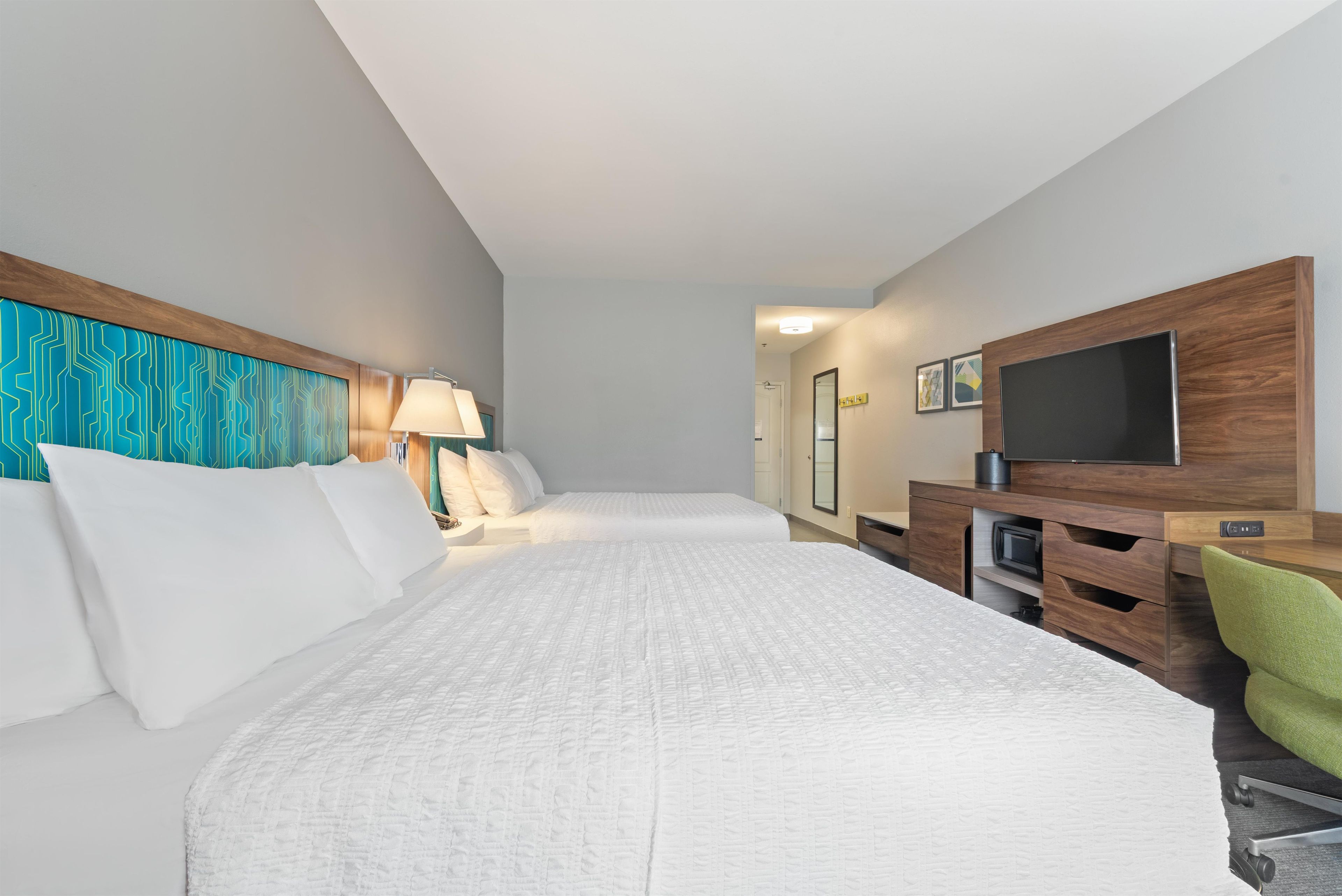 Une chambre d’hôtel avec un grand lit, un bureau doté d’un téléviseur à écran plat, une chaise et un téléviseur fixé au mur.