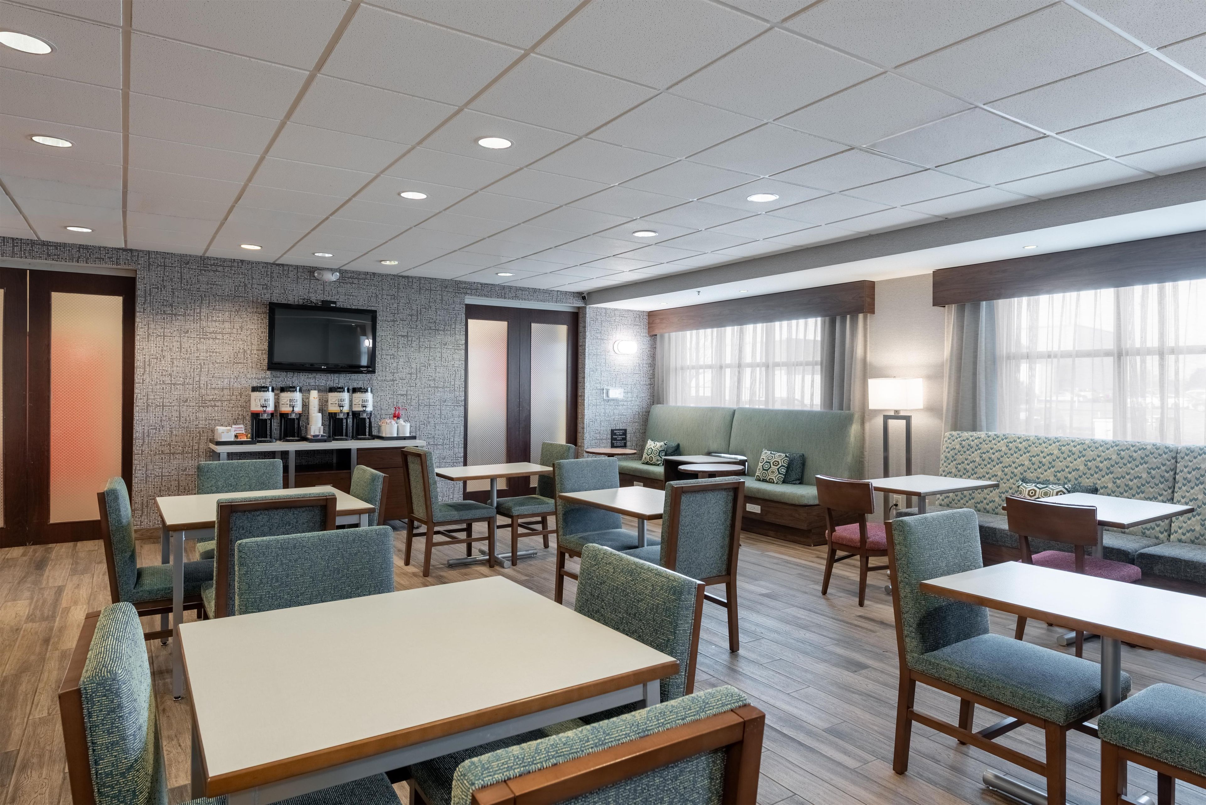A modern hotel lobby with a coffee bar, seating areas, and a television.