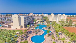 Et resort med flere swimmingpools, en stor hotelbygning og udsigt til havet.