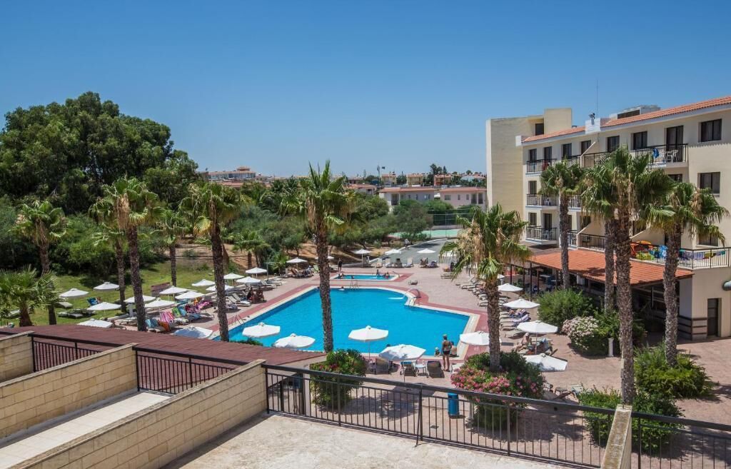 Un hotel con piscina rodeada de palmeras y tumbonas.