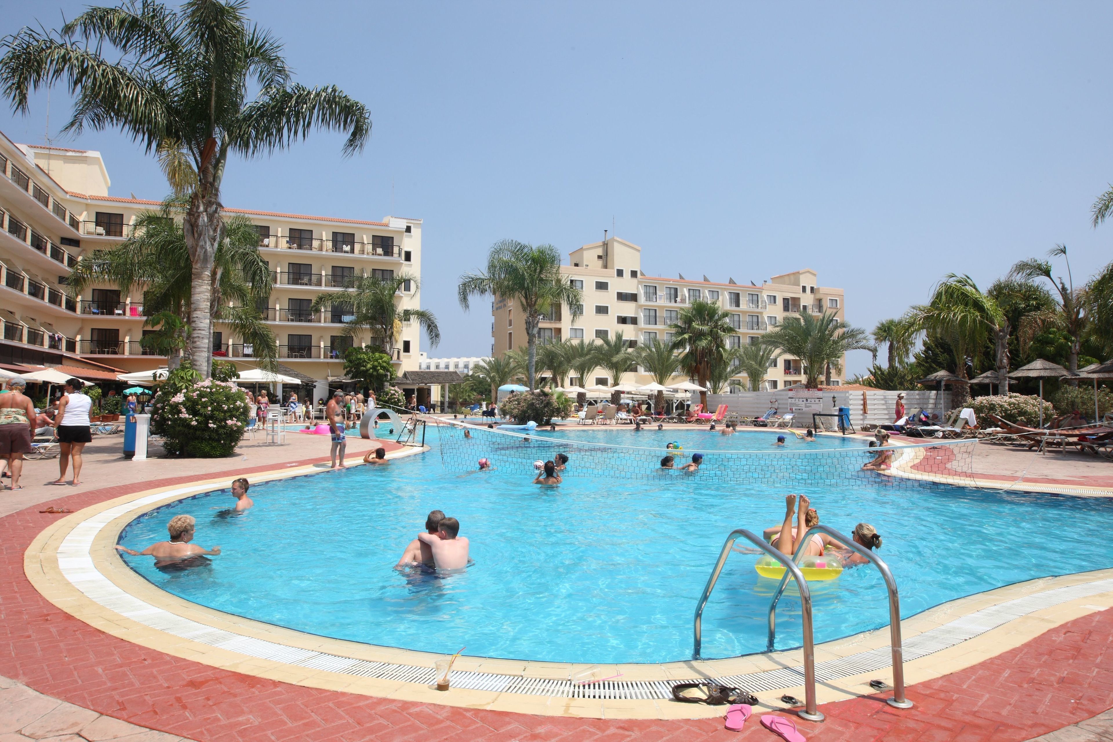 A swimming pool surrounded by palm trees and multi-story buildings with balconies.