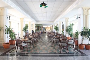 A spacious lobby with a checkered floor, wooden chairs, and potted plants. - Tsokkos Gardens Hotel (Paralimni)