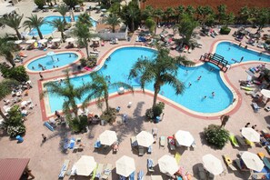 A large outdoor swimming pool with multiple lanes, surrounded by palm trees and sun loungers. - Tsokkos Gardens Hotel (Paralimni)