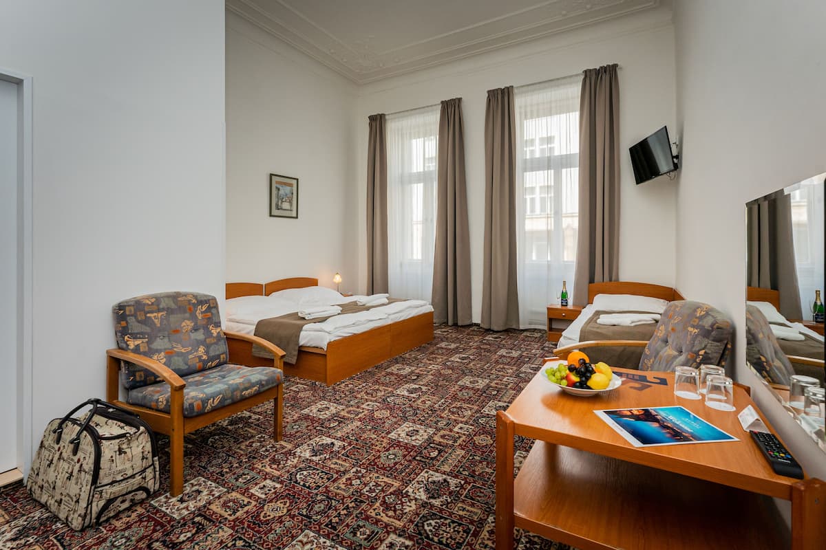 Habitación de hotel con una cama, dos sillones, una mesita con frutero, vasos y un control remoto.