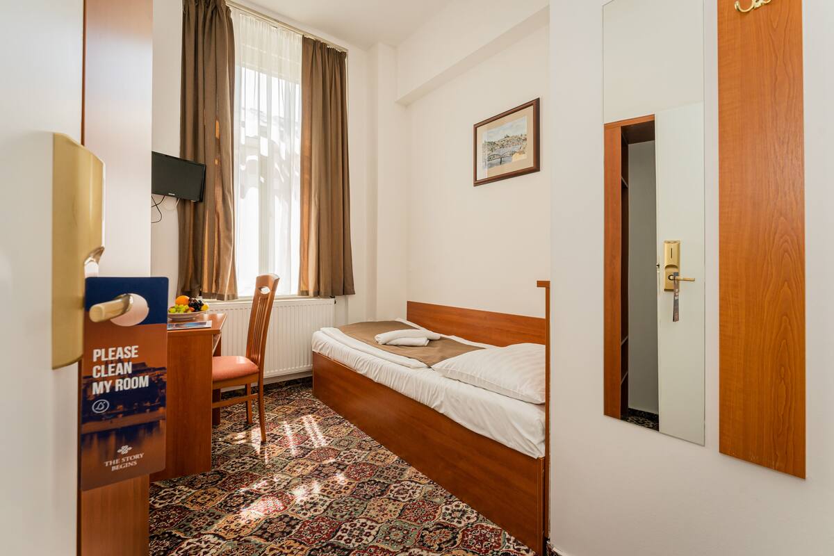 Habitación de hotel con cama, escritorio con silla, televisor montado en la pared y ventana con cortinas.