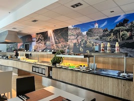 A buffet area with a waterfall mural, a chef preparing food, and a variety of fruits and beverages.