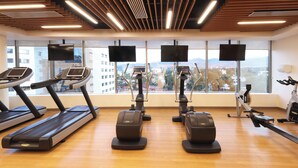 Een sportschool met loopbanden, elliptische trainers en hometrainers, grote ramen met uitzicht op de stad en een houten vloer.