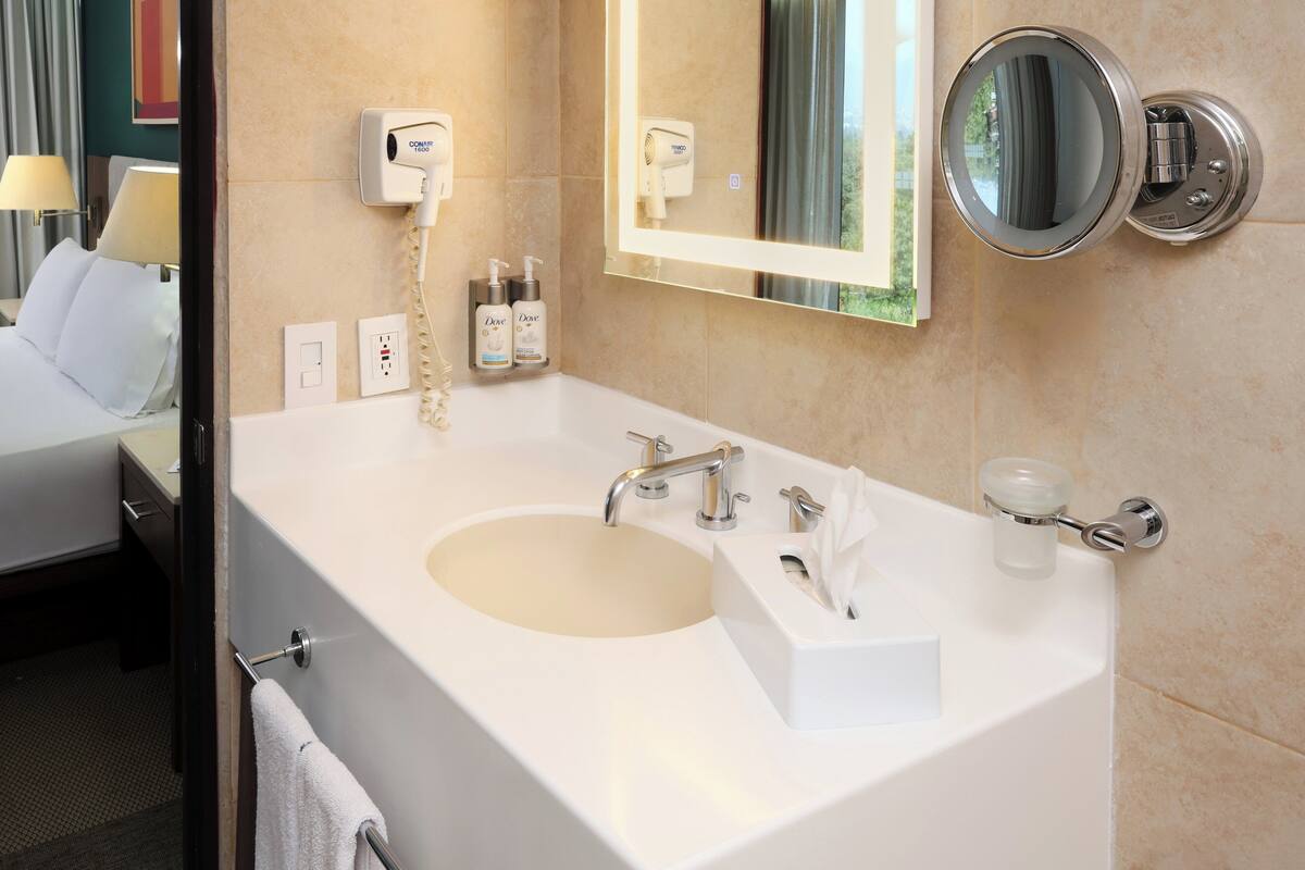 Une salle de bain d’hôtel équipée d’un grand lavabo, d’un miroir, d’un sèche-cheveux et d’articles de toilette.