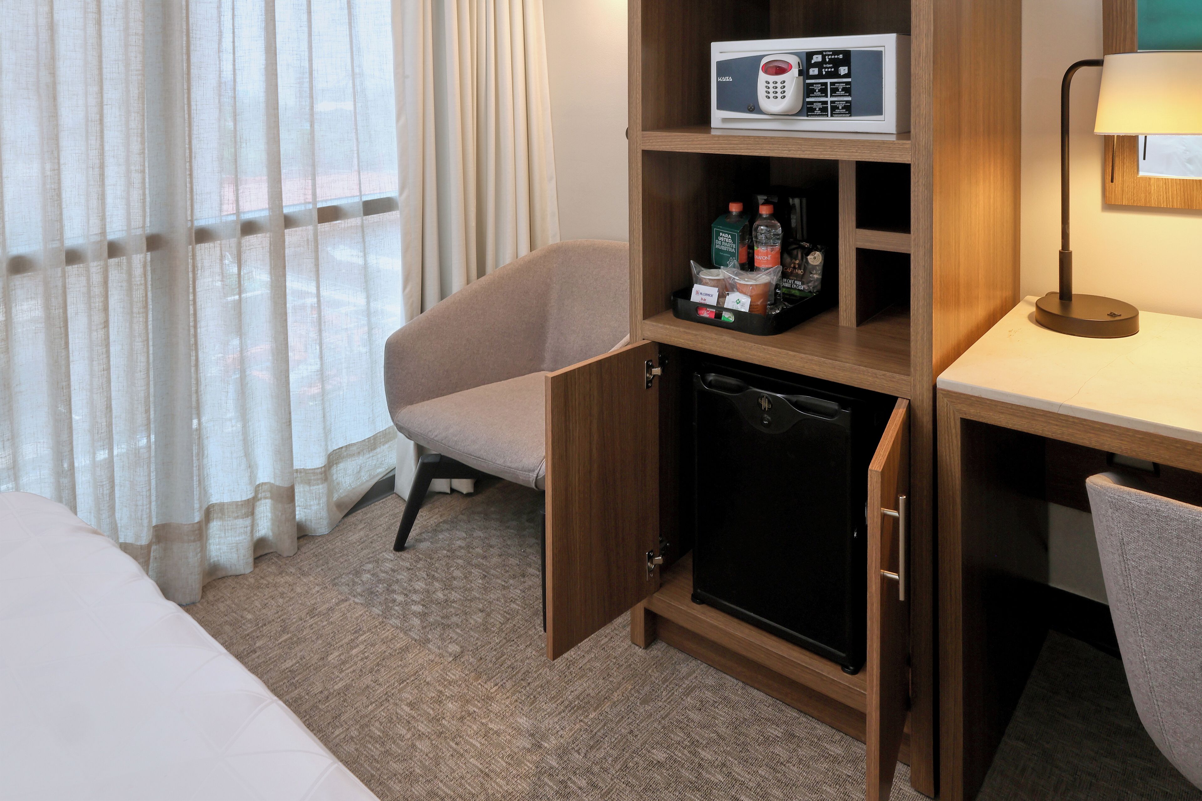 A hotel room with a bed, a desk, a minibar, a refrigerator, and a window with curtains.