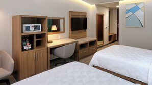 Een hotelkamer met twee bedden, een bureau met een computer en een magnetron, een televisie en een kast met toiletartikelen.