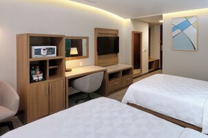 Una habitación de hotel con escritorio, dos camas, televisor y minibar.