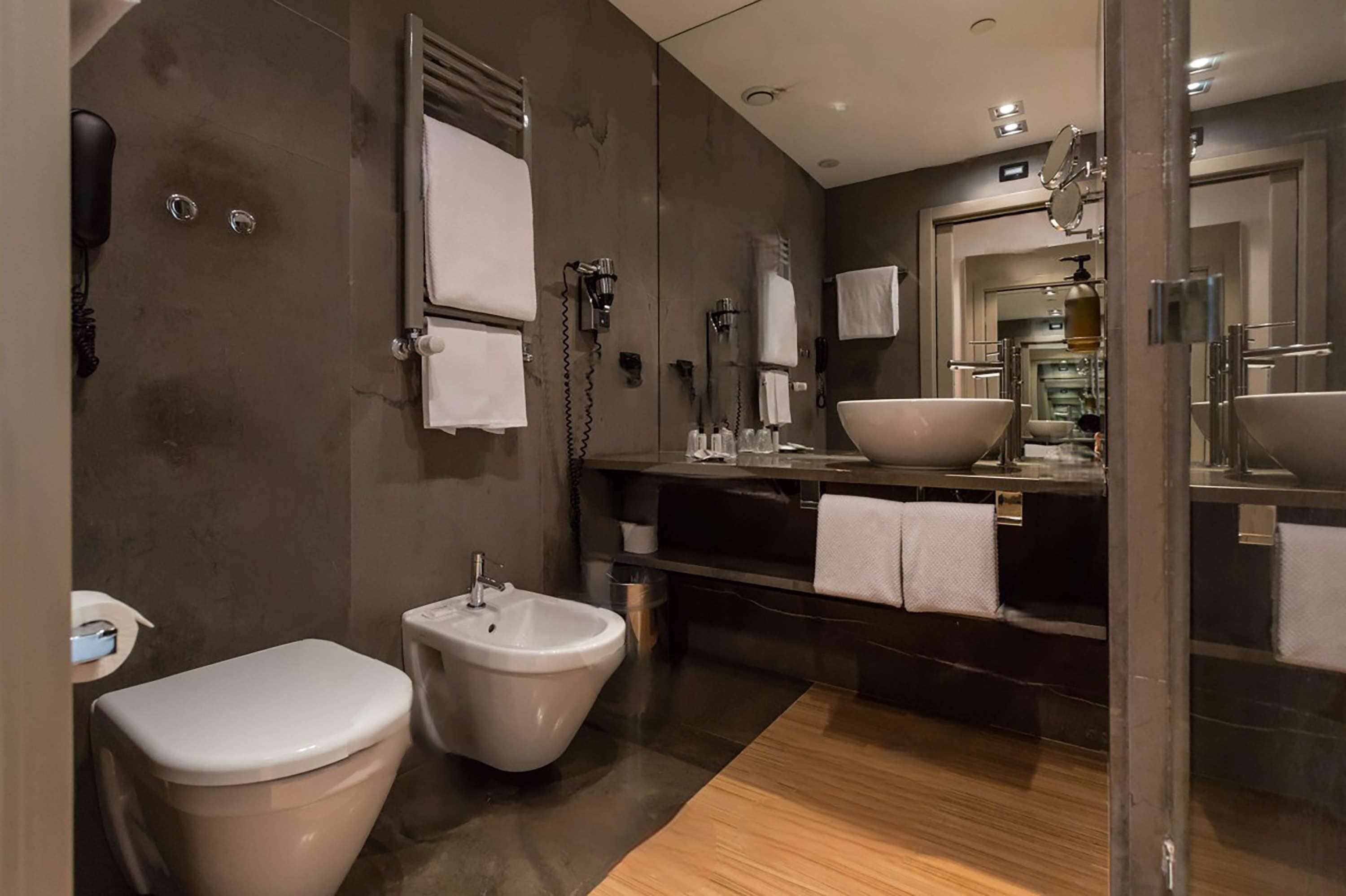 A modern bathroom with a bidet, a large mirror, and a vanity with a sink and towel rack.