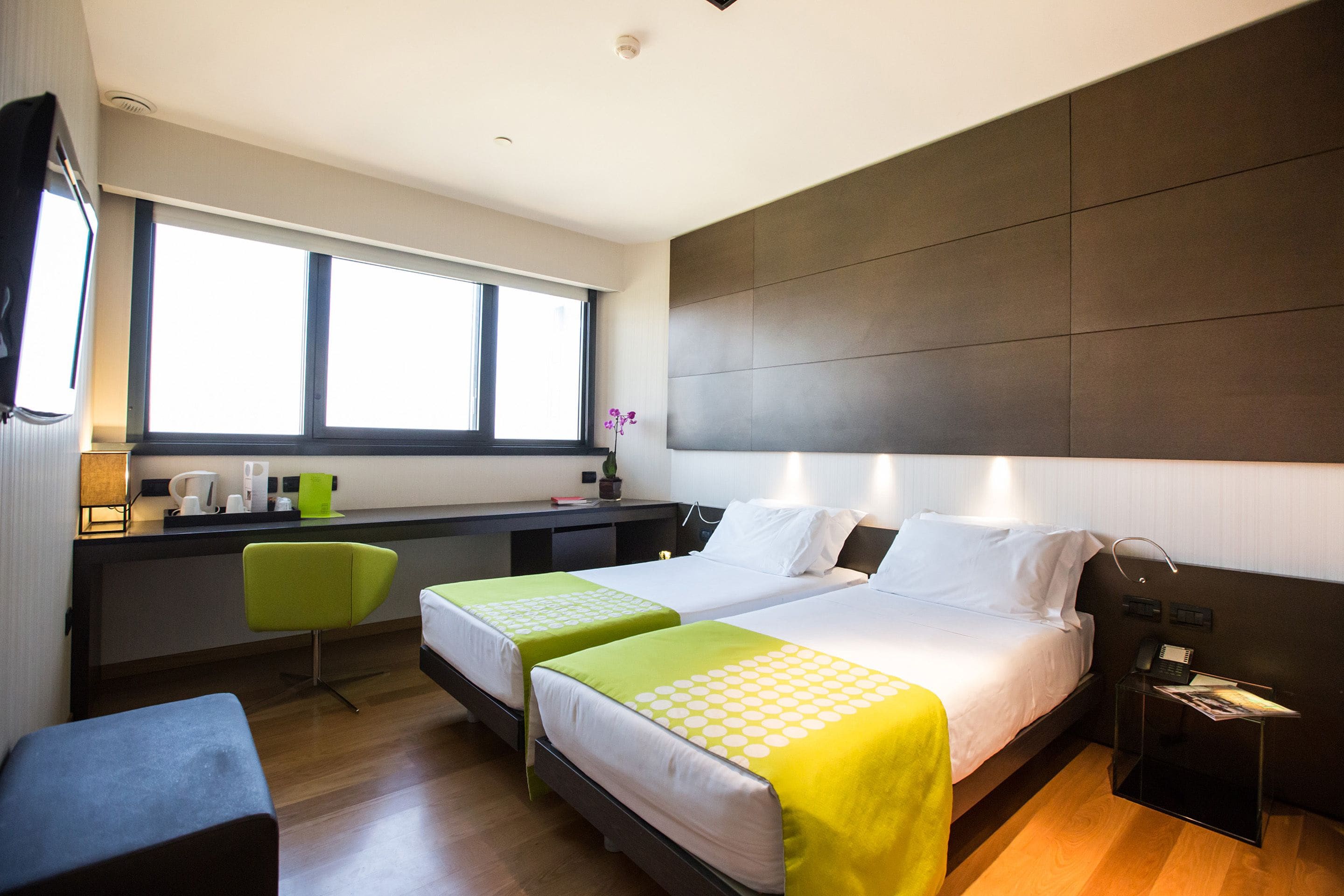 A hotel room with two beds, a desk, a chair, and a window.