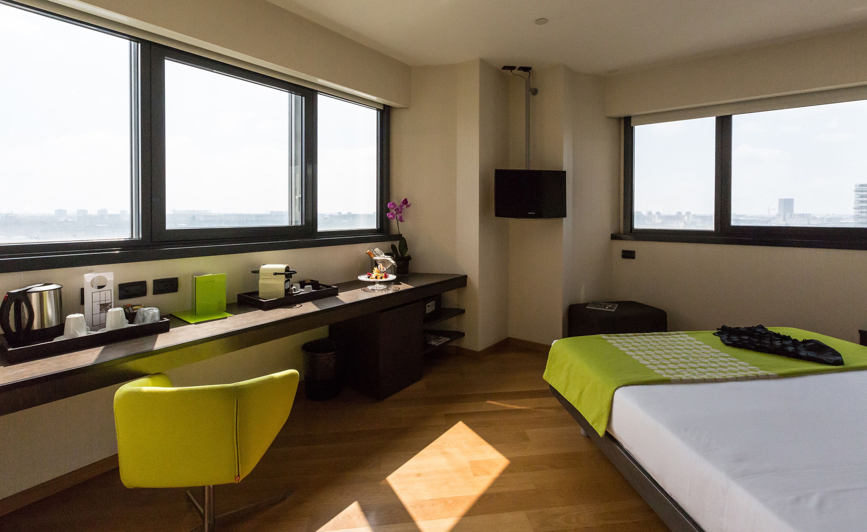 A hotel room with a desk, a chair, a bed, and a TV.