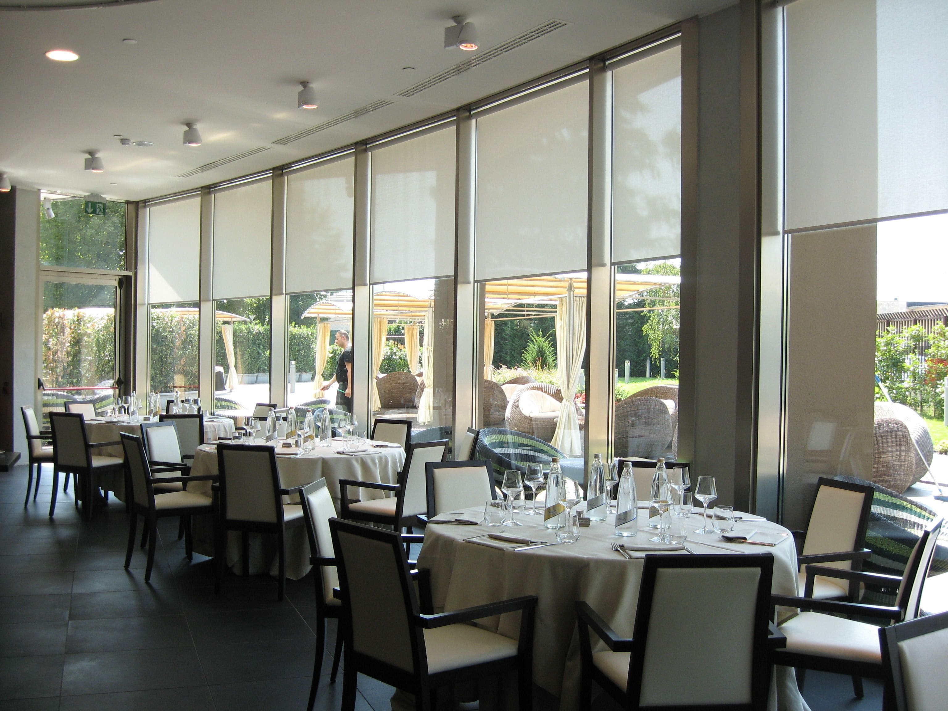 Un ristorante con ampie vetrate, tavoli apparecchiati con tovaglie bianche e sedie.
