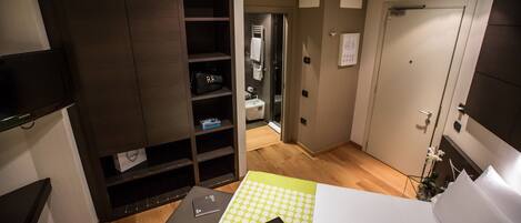 Habitación de hotel con cama, escritorio, silla, armario y baño visible a través de una puerta abierta.