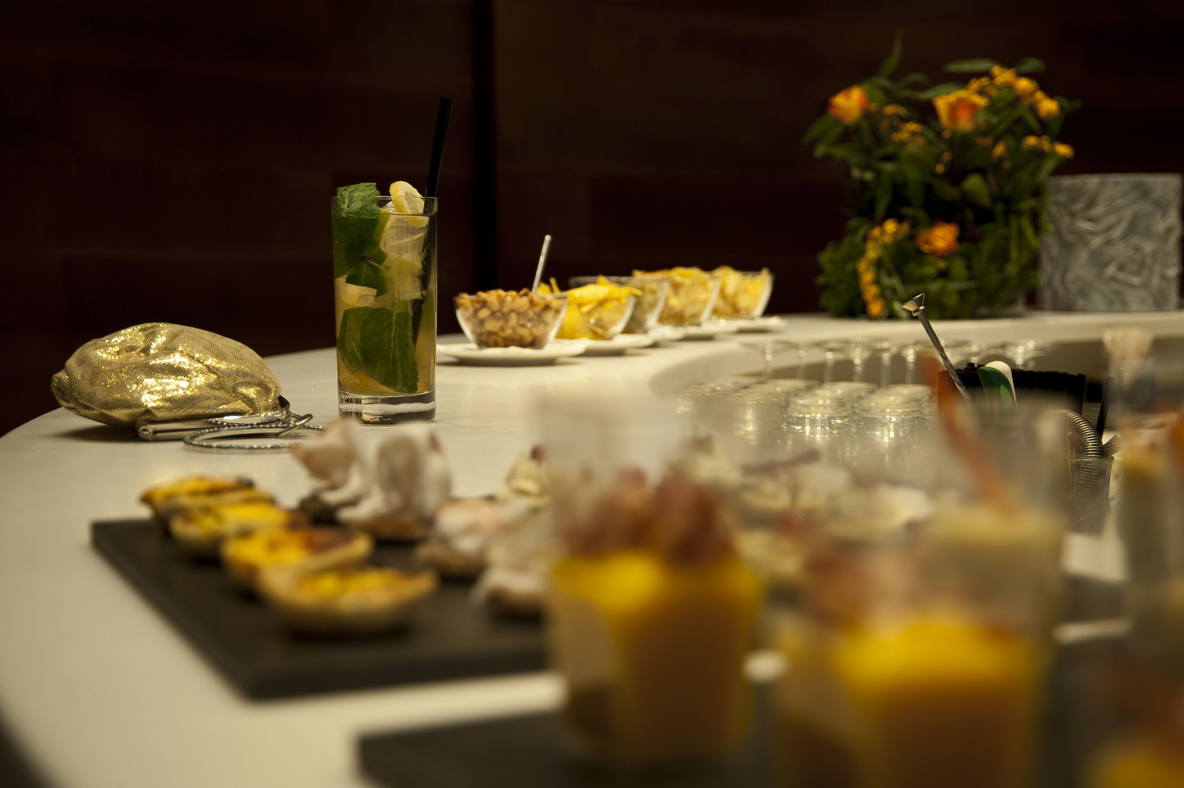 Een gedekte tafel met diverse etenswaren en drankjes, waaronder een glas met rietje en muntblaadjes, en een schaal fruit.