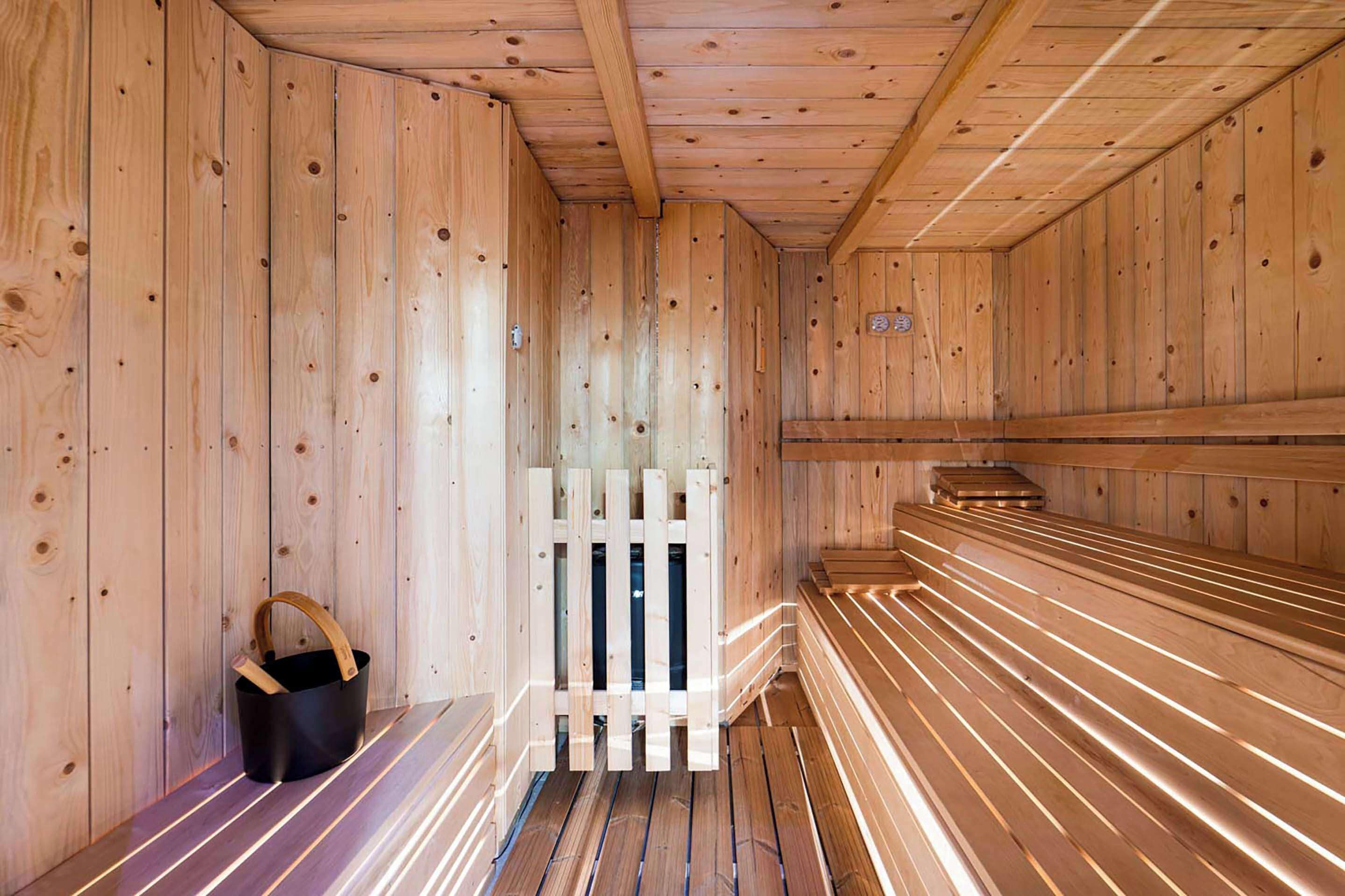 Eine Sauna mit Holzwänden und -bänken, einer Holztür und einem schwarzen Eimer mit Tragegriff.