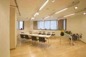 Una sala conferenze con un lungo tavolo, sedie e un tavolino con un vaso.