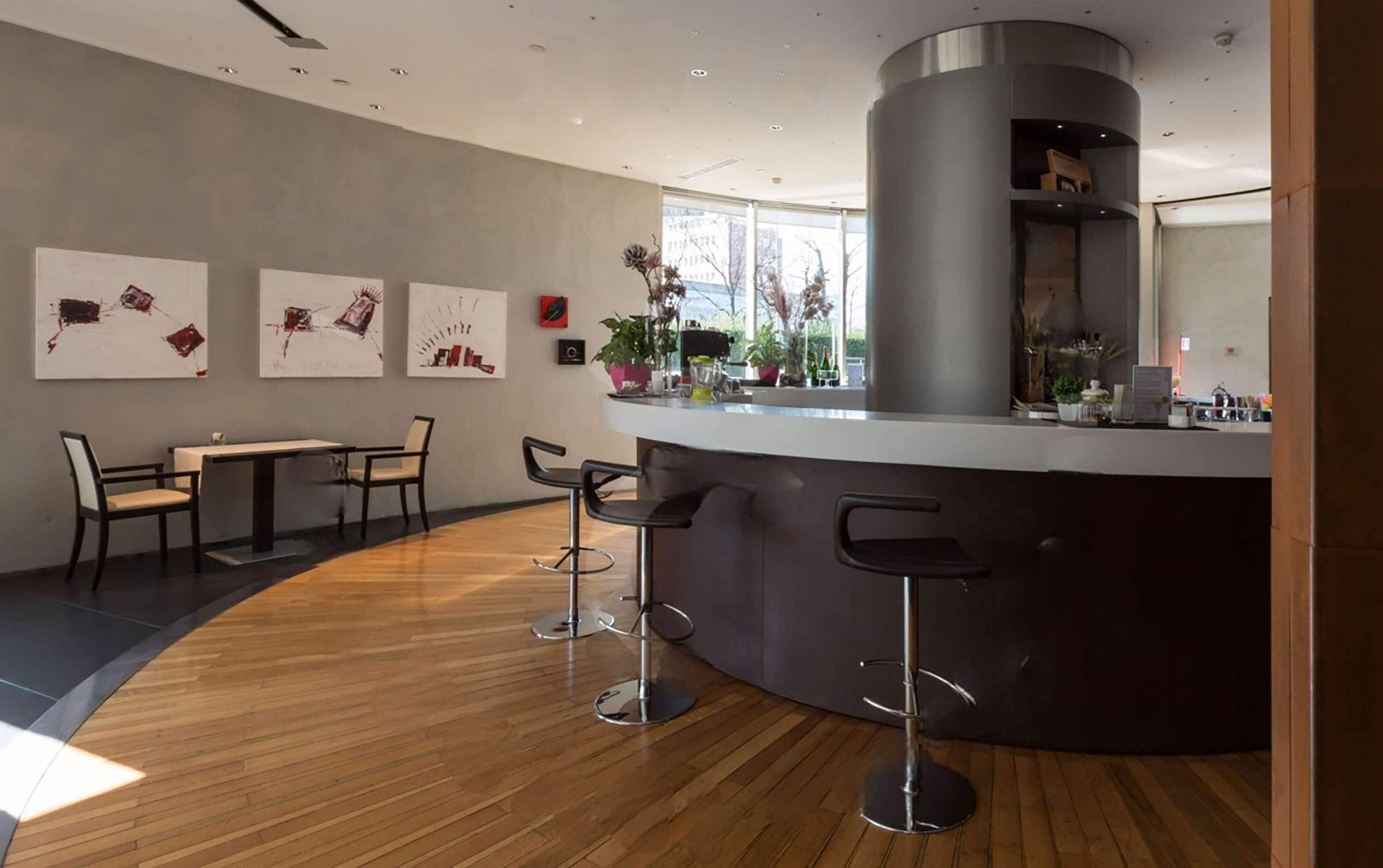 Un espace bar moderne doté d’un comptoir incurvé, de tabourets de bar et d’un coin salon avec des tables et des chaises.