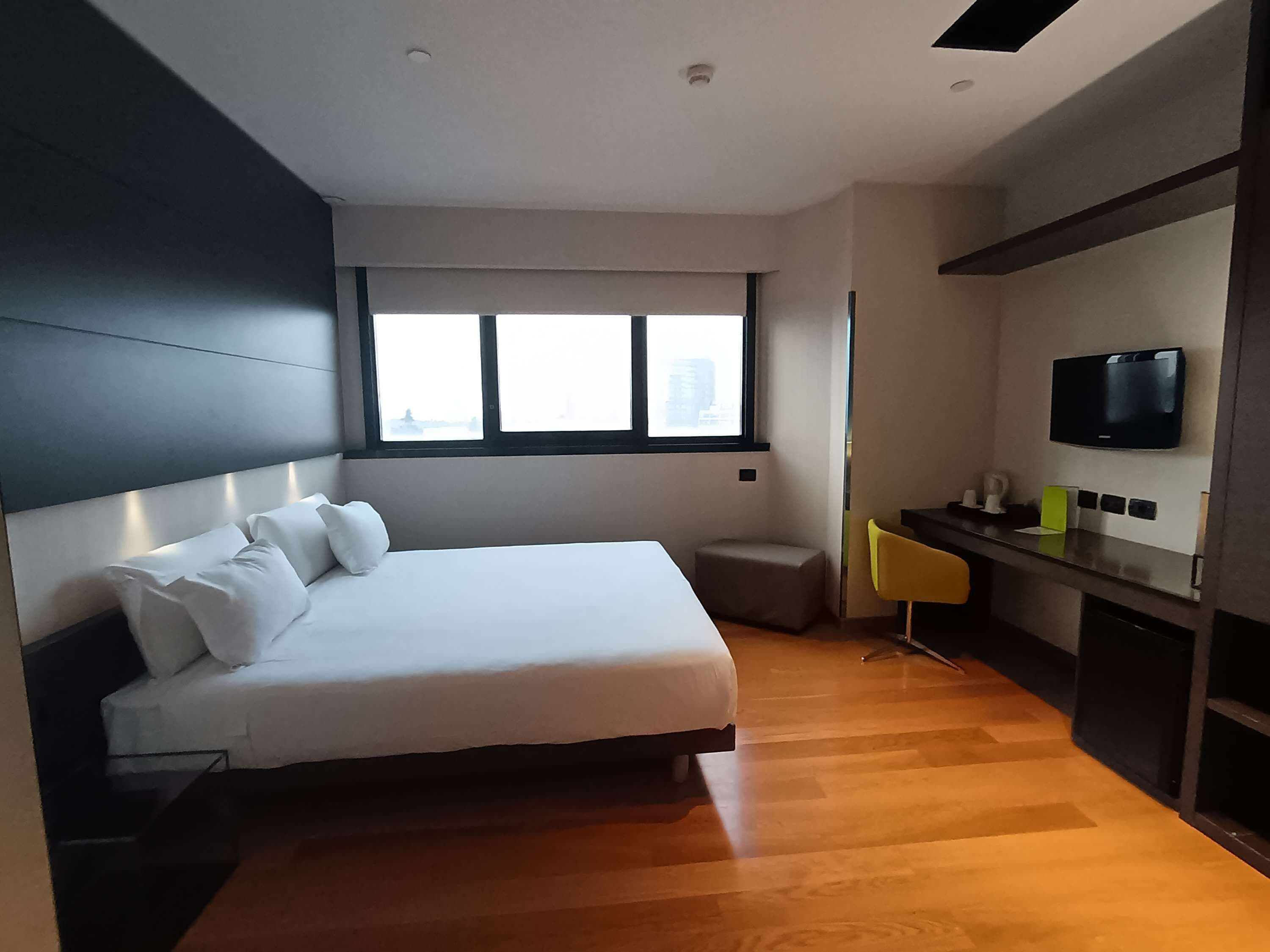 A modern hotel room with a large bed, a desk with a flat-screen TV, and a window with a city view.
