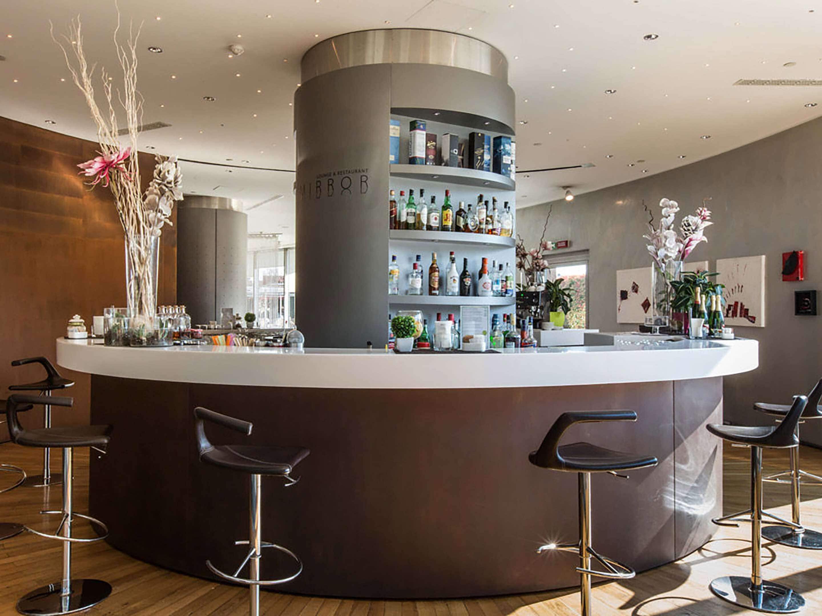 Een moderne bar met een centraal aanrecht, meerdere barkrukken en flessenrekken.