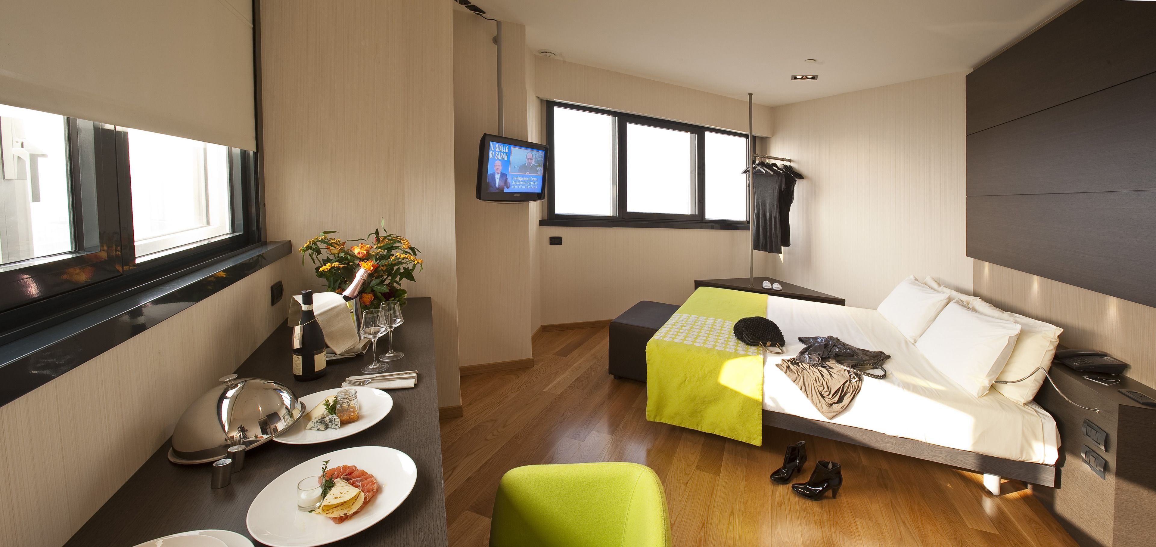 Una habitación de hotel moderna con una cama, un escritorio con provisiones para el desayuno, un televisor y una ventana con persianas.