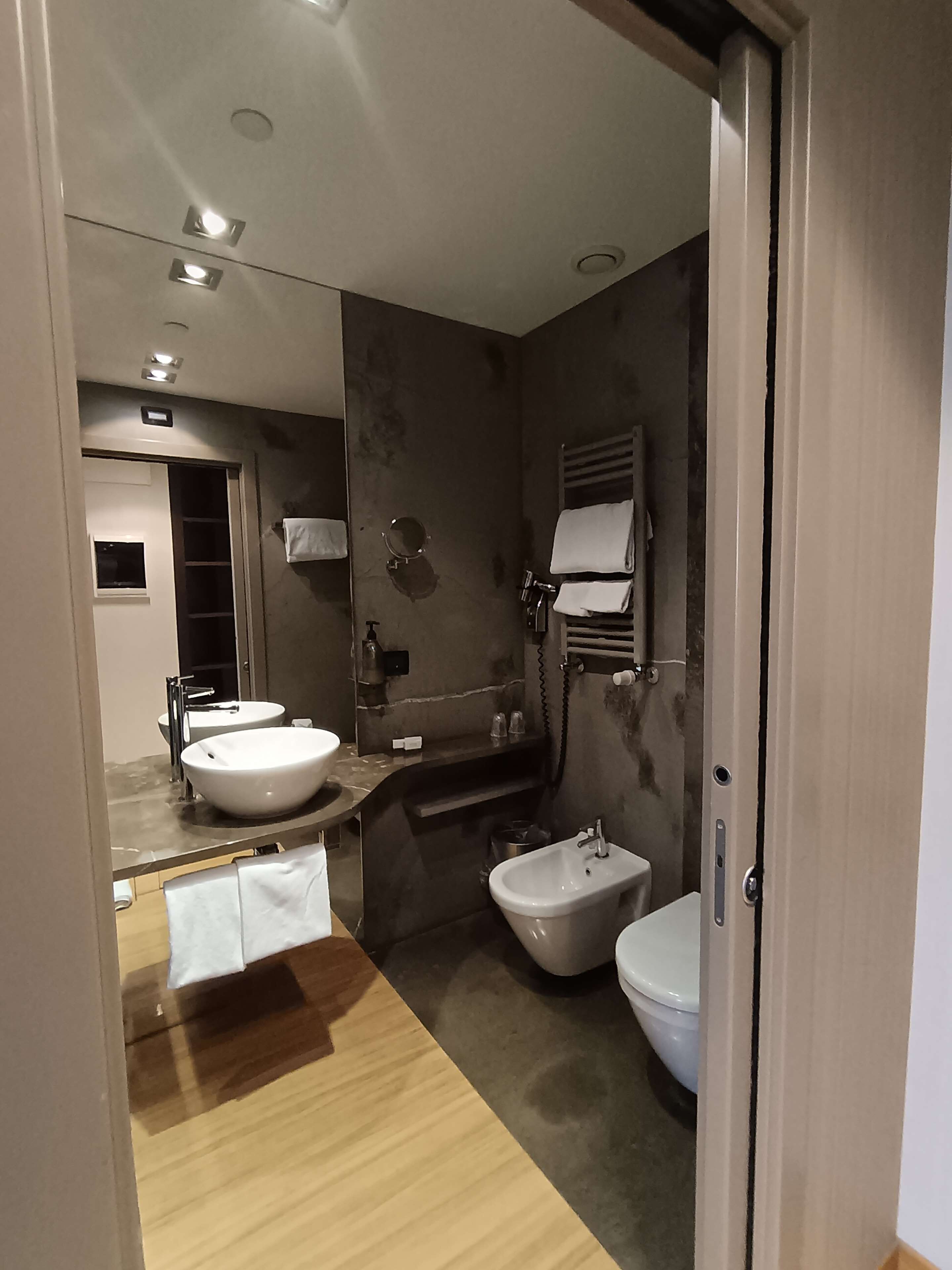 A modern bathroom with a large mirror, two sinks, a bidet, and a toilet.