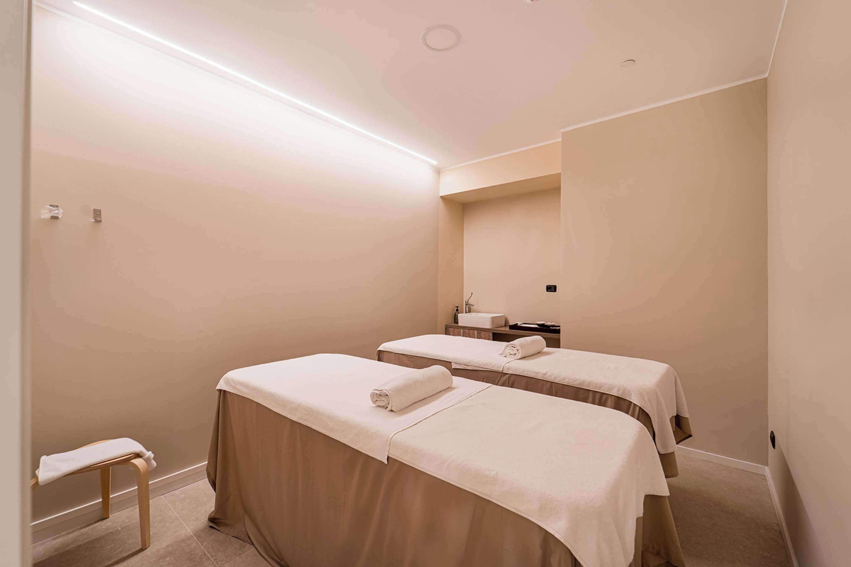 Ein Zimmer mit zwei Betten, einer kleinen Bank und einem Spiegel an der Wand.