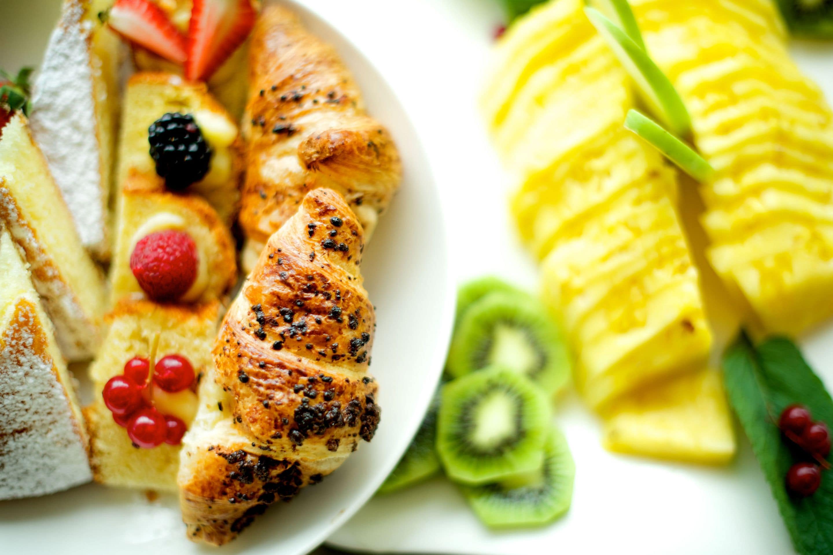 A breakfast plate with croissants, strawberries, raspberries, blackberries, kiwi slices, and pineapple.