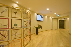 Een hotel lobby met een houten vloer, een receptiebalie en een scherm aan de muur met informatie.