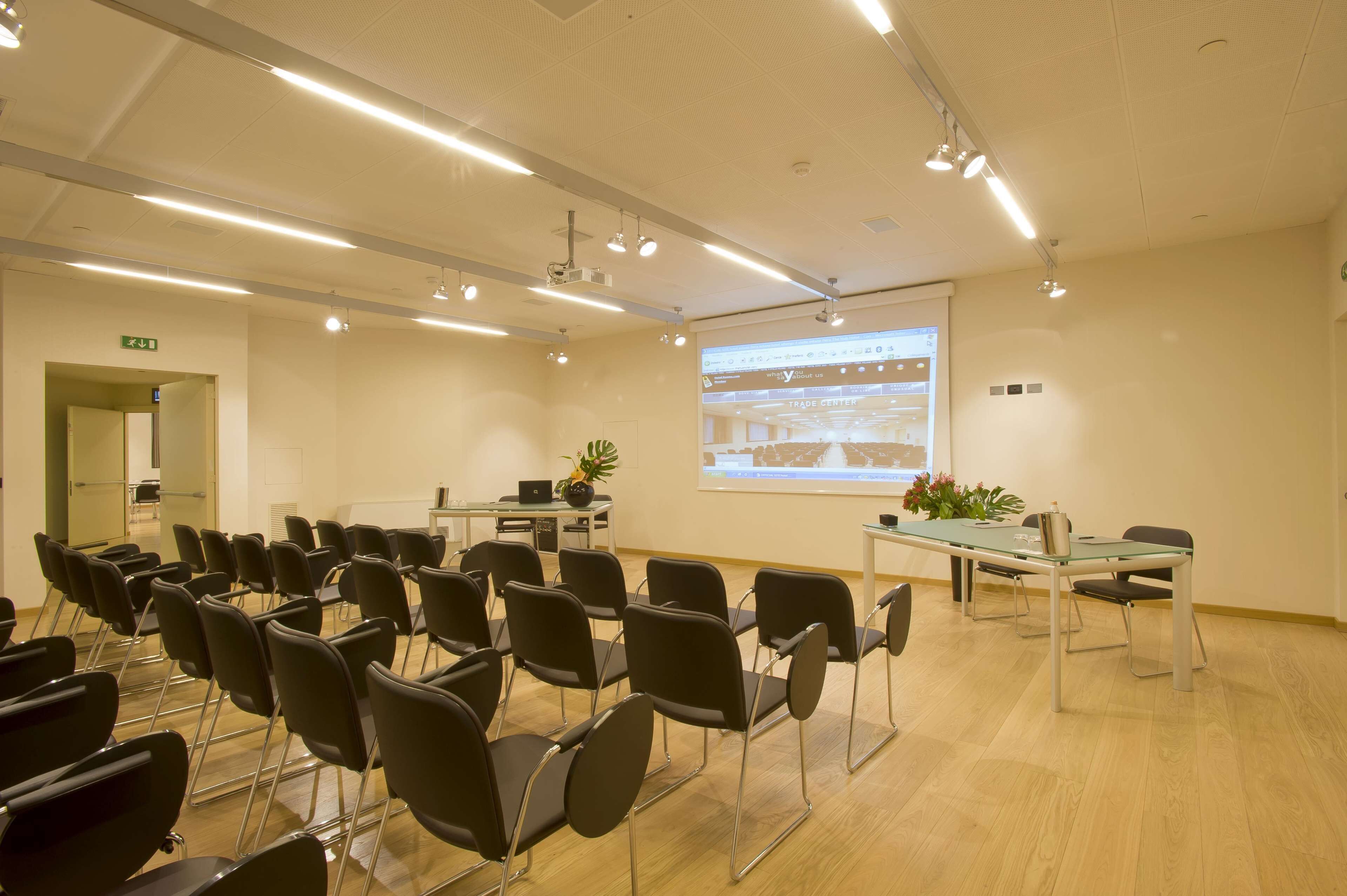 A conference room with rows of chairs, a projector screen, and a table with a laptop and a plant.