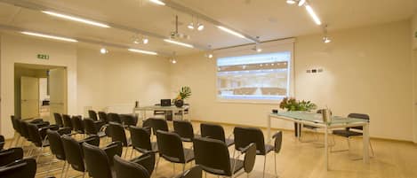 A conference room with rows of chairs, a projector screen, and a table with a laptop and a plant.